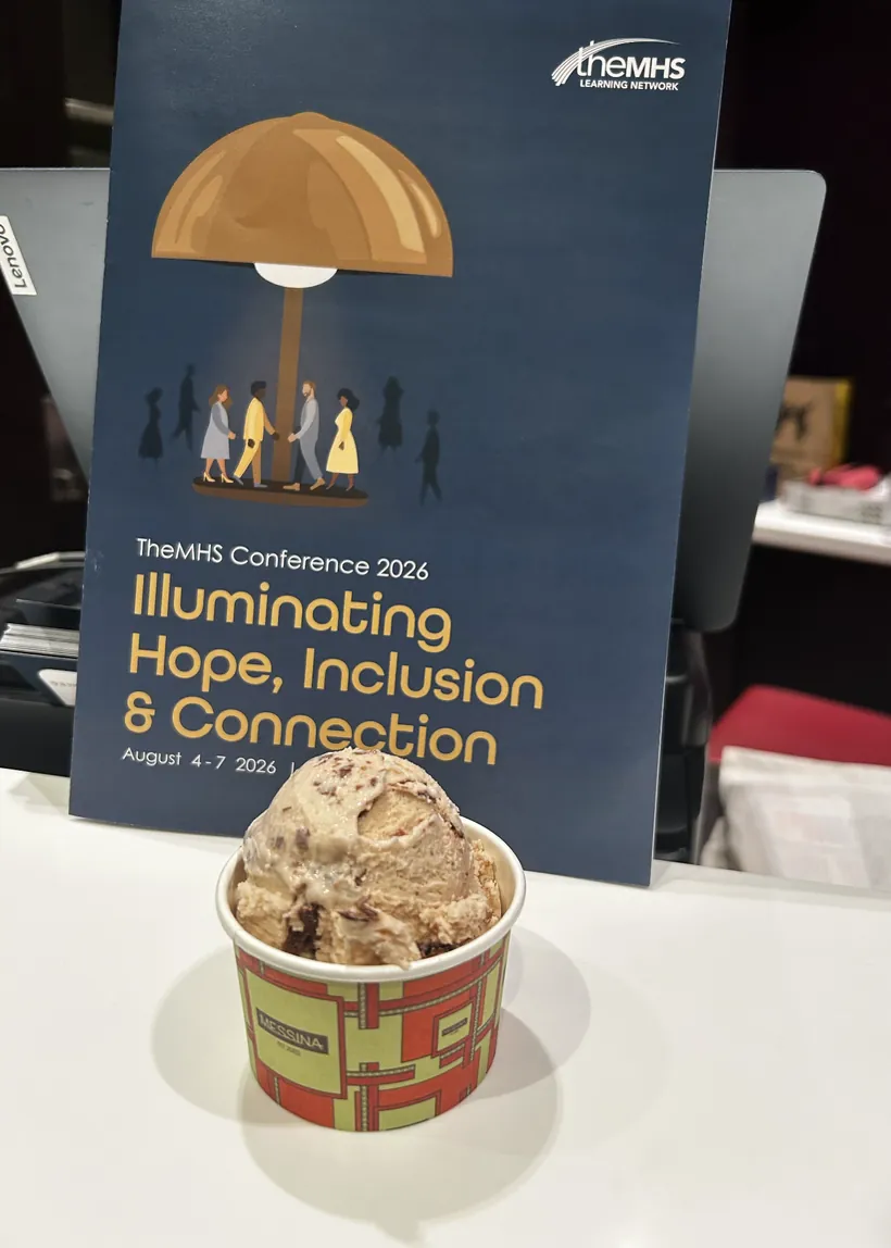 A cup of Gelato Messina in front of a TheMHS Conference 2026 Illuminating Hope, Inclusion and Connection poster