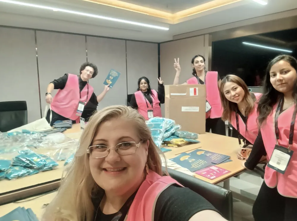 Six TheMHS conference volunteers in bright pink vests preparing delegate bags around a table